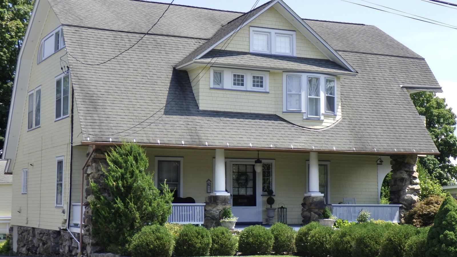 A two-story Dutch Colonial Revival house with a stone-columned front porch