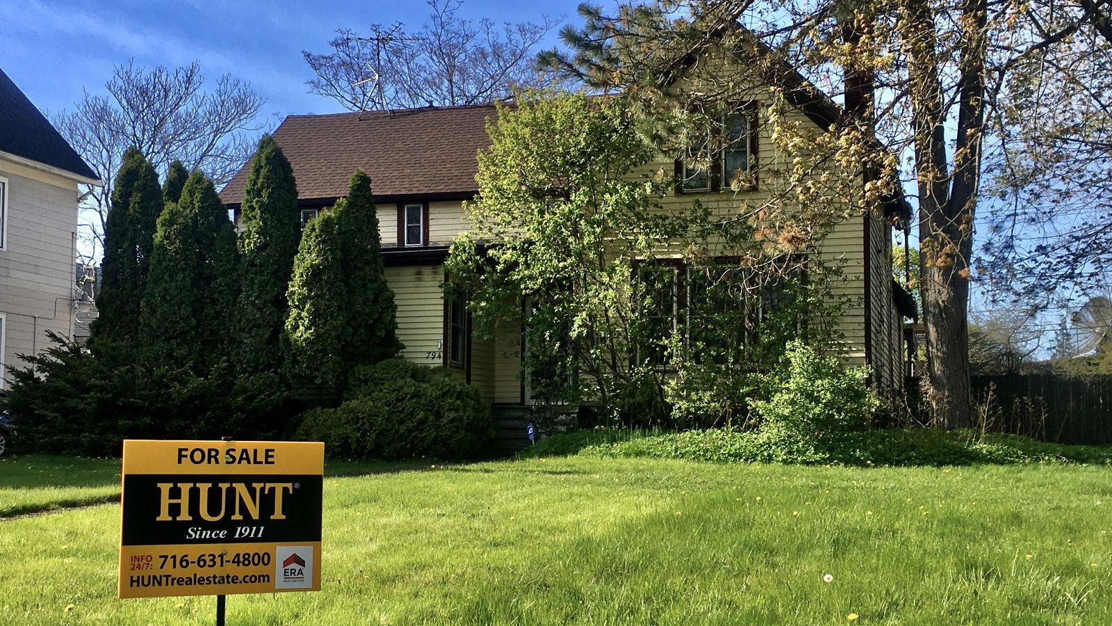 A 'For Sale' yard sign in front of a cottage with a green lawn