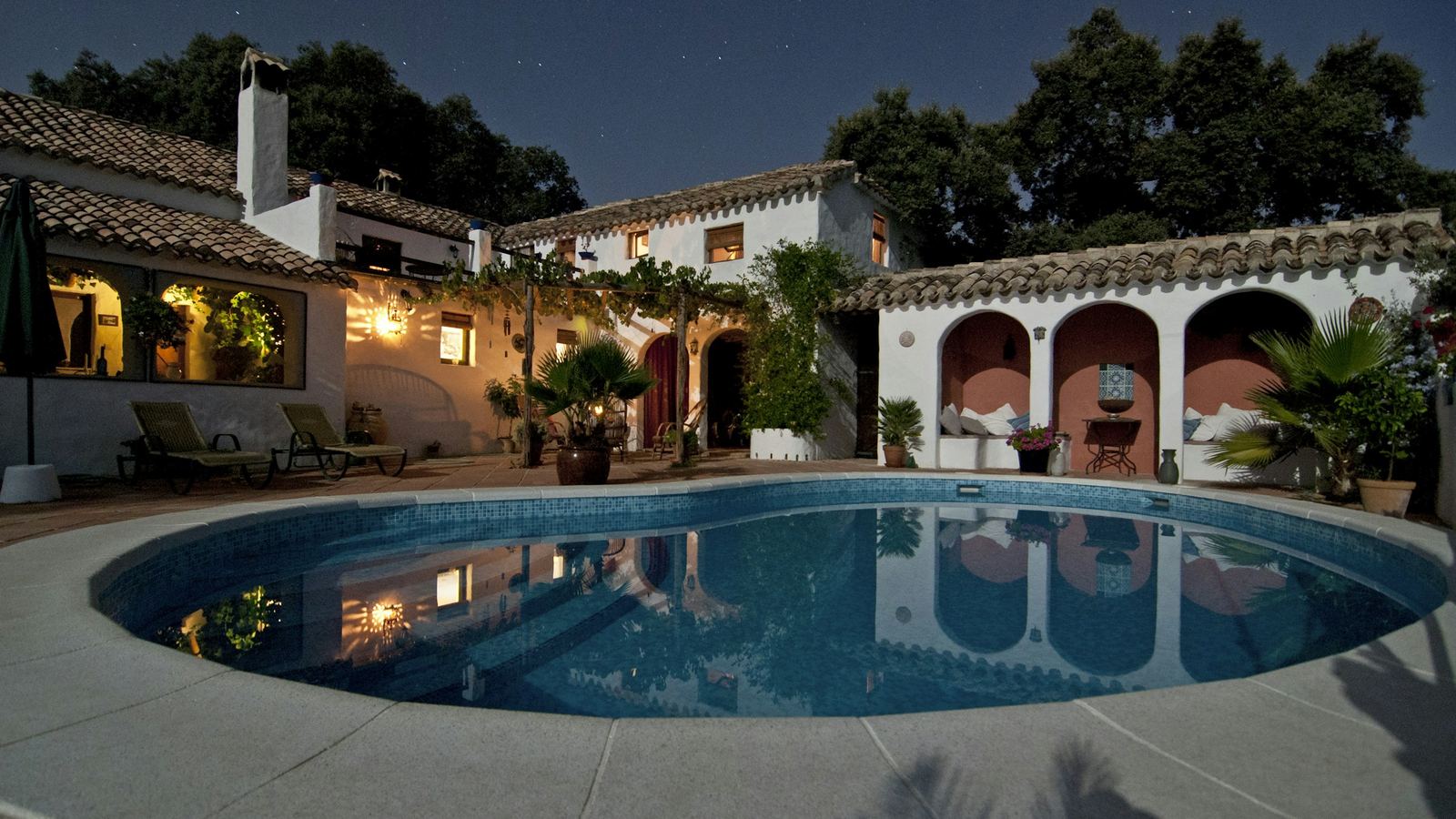 Spanish Colonial-style house with a lit courtyard pool at night