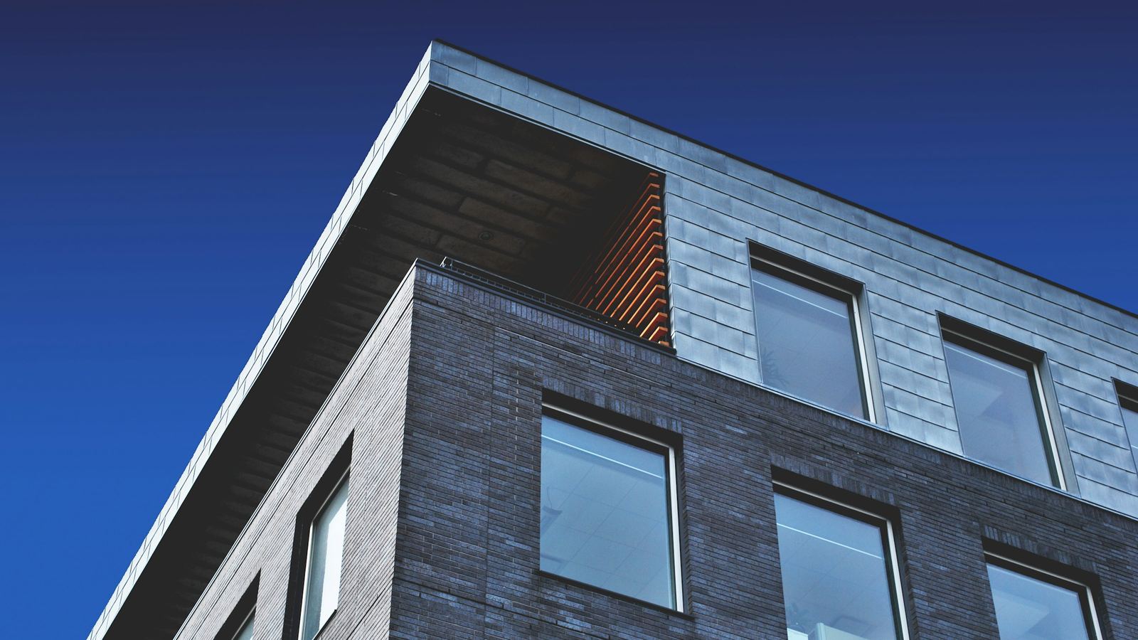 Modern brick multifamily building seen from below against a blue sky