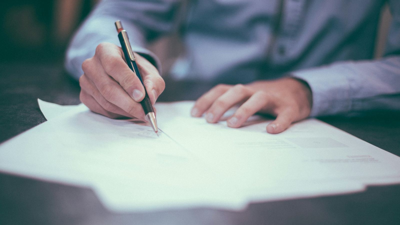 A person signs a paper document at a desk
