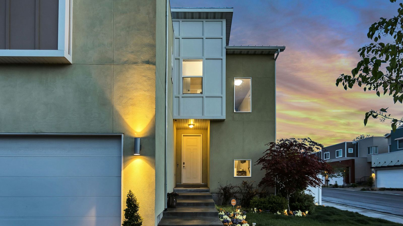 Contemporary two-story house with its entry lights on at dusk