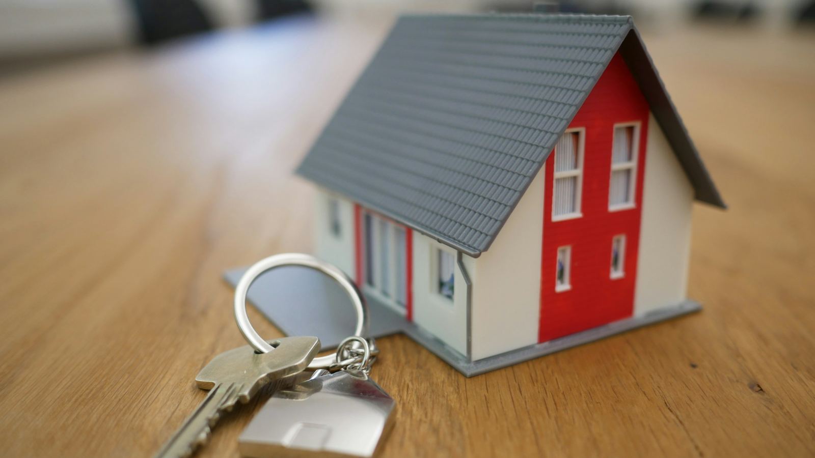 A small model house beside a set of house keys on a wooden table