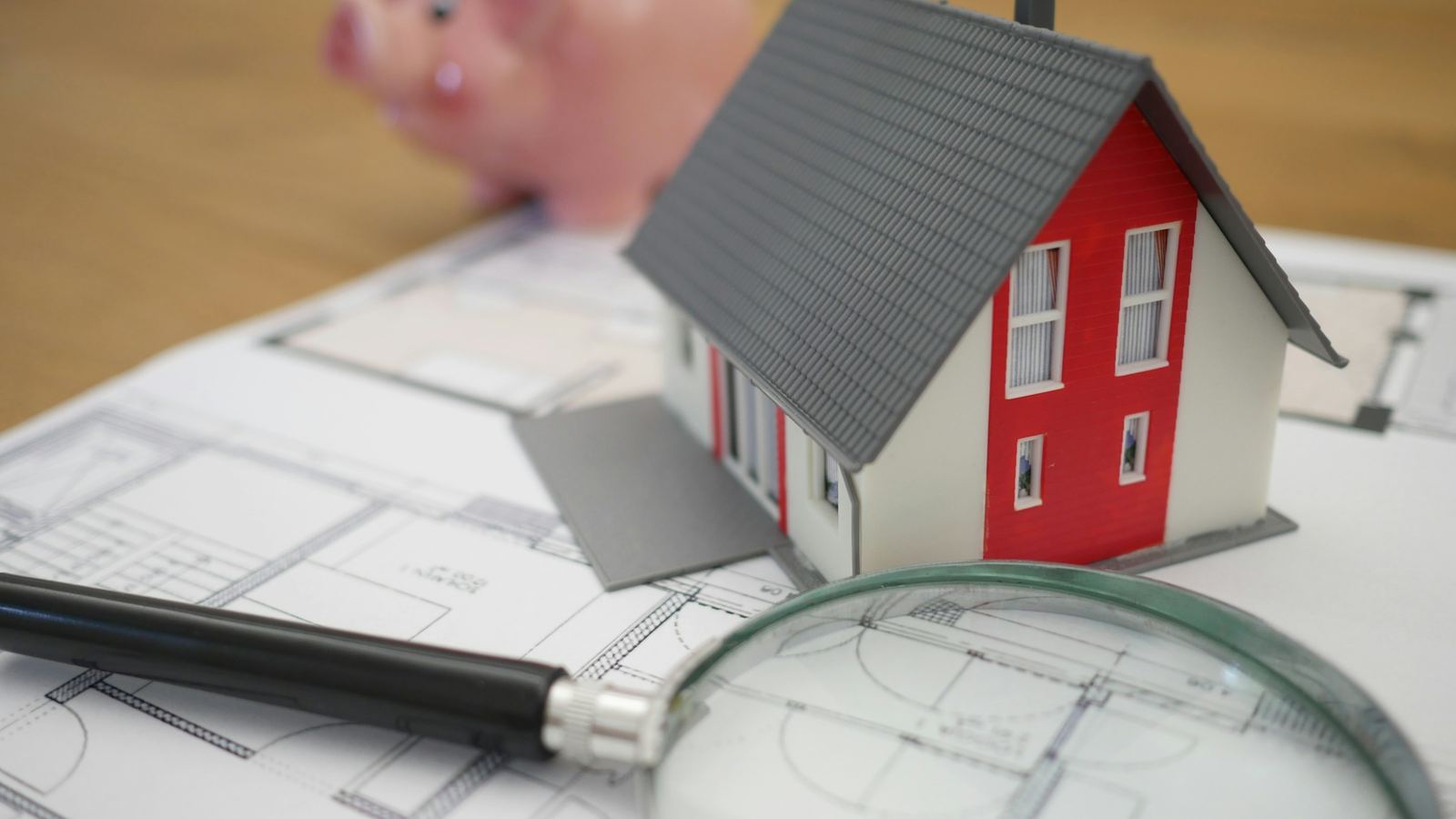 Model house, magnifying glass and piggy bank on a floor plan