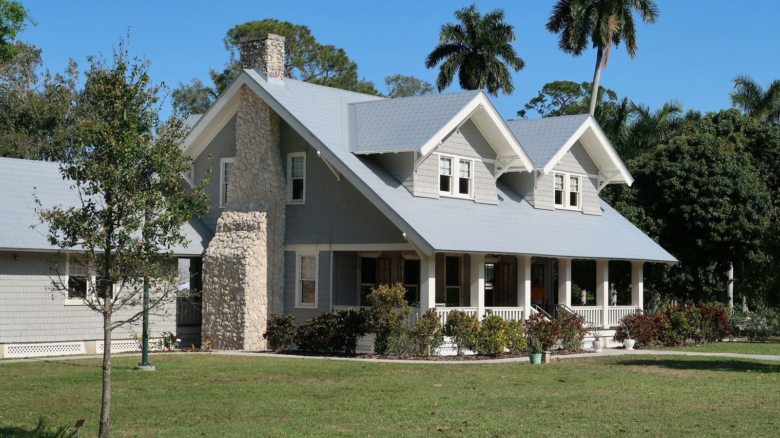 Gray single-family house with a stone chimney and palm trees